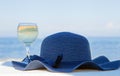 A glass of white wine and a blue hat behind lagoon sea. Summer vacation concept.Beautiful summer day sea view. Luxury