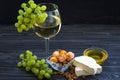A glass of white wine with cheese cuts, figs, nuts, honey, grapes on a dark rustic wooden boards background Royalty Free Stock Photo
