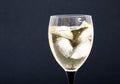 A glass of white wine with pieces, ice cubes. Wine with ice on a black background. Glass with a black  leg Royalty Free Stock Photo
