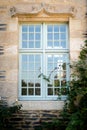 Glass window on the stone facade of a mansion. Wild roses decorate the wall of the classical building Royalty Free Stock Photo