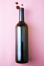 Glass wine bottle and drops of red wine on a pink background Royalty Free Stock Photo