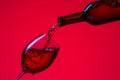 Glass of Wine and Bottle with Pouring Out Liquid. Against Red Royalty Free Stock Photo