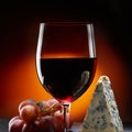 Glass of wine with grapes and a piece of cheese with mold. Orange background. Royalty Free Stock Photo