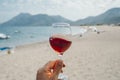 Glass of wine in hand. A glass of red wine against the background of the Mediterranean beach and the sea in a tourist Royalty Free Stock Photo