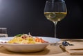 Glass with wine near delicious spaghetti pasta with shrimps, grated cheese, jamon, tomato sauce and basil in white plate