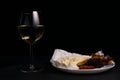 glass of wine next to a slice of cheese, plums on a black background Royalty Free Stock Photo