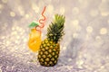 A glass of yellow drink with ice and ripe pineapple on a gray glittering background