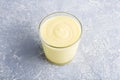 Glass of yellow mango or banana yogurt or smoothie on gray background. Turmeric Lassie lassi. Healthy dairy snack. Copy space