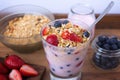 Glass with yogurt, cereals, strawberries and blueberries on wooden table - closeup