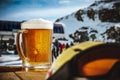 Glasse of beer on wooden table in outdoor cafe with snowy mountain background.