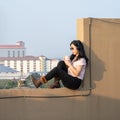 Glasses Asian woman is listening music via headset, drinking coffee on rooftop barricade cement not dangerous because the Royalty Free Stock Photo