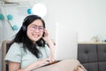 Glasses beautiful Asian woman is working on her laptop in the bedroom with a pastel green - brown color theme Royalty Free Stock Photo