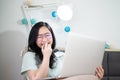 Glasses beautiful Asian woman is working from home with her laptop in the bedroom with a pastel green - brown color theme Royalty Free Stock Photo