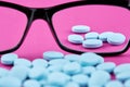 Glasses and blue pills on pink background. Medicine