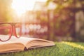 Glasses and book on green grass with blur and bokeh in sunrise t Royalty Free Stock Photo