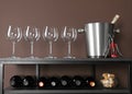 Glasses, bucket, corkscrew and bottles of wine on rack near brown wall Royalty Free Stock Photo
