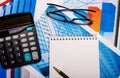 Glasses, a calculator, a blank notebook and a pen are on the bright diagrams. Workplace close up Royalty Free Stock Photo