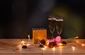 Glasses with champagne, christmas gift, strawberry macaroons, chocolate cookies and glowing christmas lights on dark background