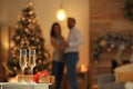 Glasses with champagne and Christmas gift on table and couple in room, bokeh effect. Space for text Royalty Free Stock Photo