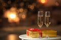 Glasses with champagne and Christmas gift on table in room, bokeh effect. Space for text Royalty Free Stock Photo