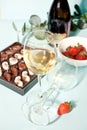Glasses of champagne or white grape wine with plate of chocolates and strawberry, bottle on the background