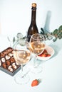 Glasses of champagne or white grape wine with plate of chocolates and strawberry, bottle on the background