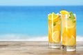 Glasses of citrus refreshing drink on wooden table near sea