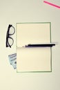 Glasses on a clean notebook pages on white table background pink red blue black white color pencils dollars money is all
