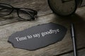 Glasses,clock,pen and a piece of black paper written with Time to say goodbye on wooden background