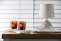 Glasses of cold drink with stylish cup coasters, lamp and stationery on wooden table in room Royalty Free Stock Photo