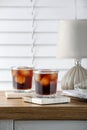 Glasses of cold drink with stylish cup coasters, lamp and stationery on wooden table in room Royalty Free Stock Photo