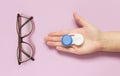 Glasses and contact lens case in human hand on purple background. Concept of choice the way vision correction