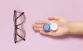 Glasses and contact lens case in human hand on purple background. Concept of choice the way vision correction