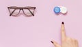 Glasses and contact lens case on purple background. Human hand indicate on lenses. Concept of choice the way vision