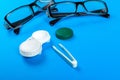 glasses, contact lenses in containers and tweezers on blue background