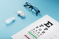 Glasses with Contact Lenses, drops and an Optometrist`s Eye Test Chart On a Blue Background Royalty Free Stock Photo