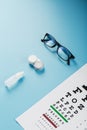 Glasses with Contact Lenses, drops and an Optometrist`s Eye Test Chart On a Blue Background Royalty Free Stock Photo