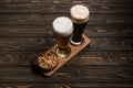 Glasses of dark and light beer near bowl with roasted peanuts on wooden table. Royalty Free Stock Photo