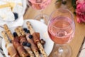 Glasses of delicious rose wine, flowers and food on wooden board, closeup Royalty Free Stock Photo