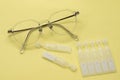 Glasses and disposable eye drops isolated on yellow background Royalty Free Stock Photo