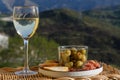 Glasses of dry white wine and spanish tapas olives in bowl with mountains peaks on background in sunny day Royalty Free Stock Photo