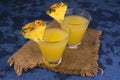 Two glasses of freshly squeezed pineapple juice on a blue background. Royalty Free Stock Photo