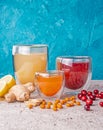 Glasses of fruit hot or cold drink tea of ginger, lemon, sea buckthorn, lingonberry. Fresh fruits and berries. Blue background