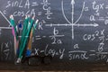 Glasses and a glass with pencils on chalkboard background with formulas. Teacher's day concept and back to school