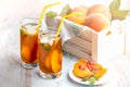 Glasses with homemade ice tea, peach flavored. Freshly cut peach slices for arrangement. White crate full with peaches in the back Royalty Free Stock Photo