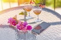 Glasses with homemade liqueur, decorative with fresh summer surreal flowers and mobile phone. Feminine flat lay. Summer