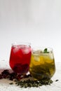 Glasses of iced green herbal tea and red hibiscus tea with dry leaves and flowers on a white table. Royalty Free Stock Photo