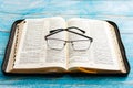 Glasses lie on the open bible, blue background