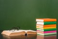 Glasses lying on the book near empty green chalkboard