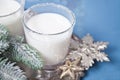 Glasses of milk, christmas tree branch, snowflake on the metal tray on the blue background